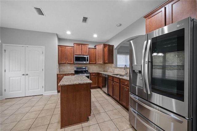 kitchen featuring a kitchen island, appliances with stainless steel finishes, sink, light tile patterned floors, and light stone counters