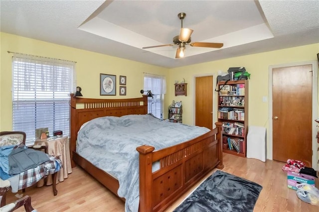 bedroom with a tray ceiling, ceiling fan, and light wood-type flooring