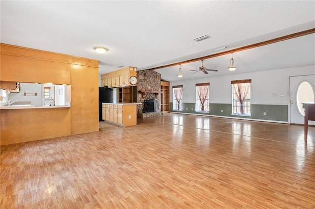 unfurnished living room with ceiling fan, a fireplace, light hardwood / wood-style floors, and vaulted ceiling with beams