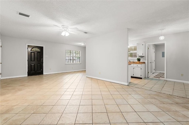 unfurnished living room featuring ceiling fan, a textured ceiling, and light tile patterned floors