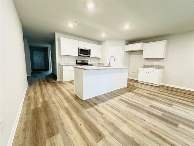 kitchen featuring light stone counters, light hardwood / wood-style flooring, appliances with stainless steel finishes, a kitchen island with sink, and white cabinets