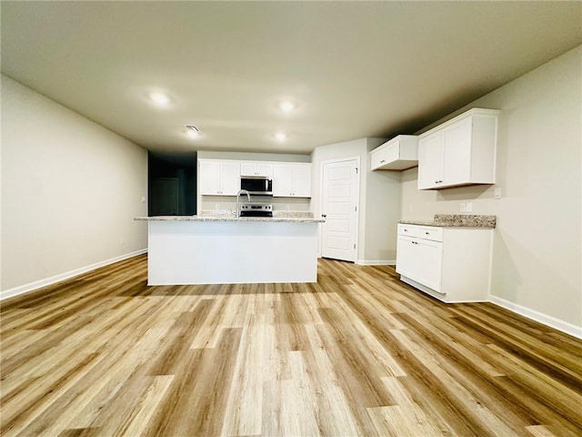 kitchen with white cabinetry, light stone countertops, stainless steel appliances, and an island with sink