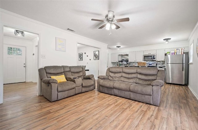 living room with ceiling fan, crown molding, and light hardwood / wood-style flooring