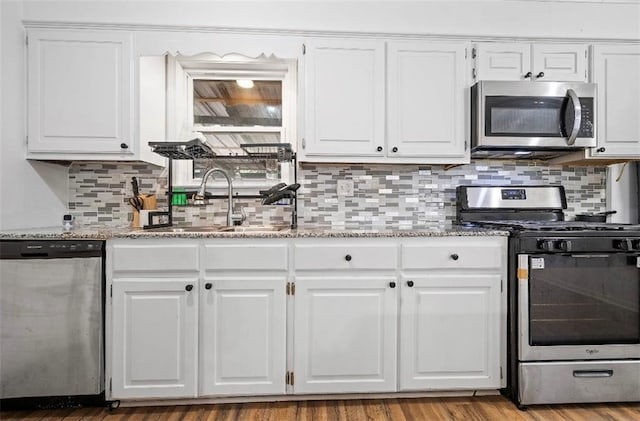 kitchen with appliances with stainless steel finishes, decorative backsplash, light stone countertops, white cabinets, and hardwood / wood-style flooring