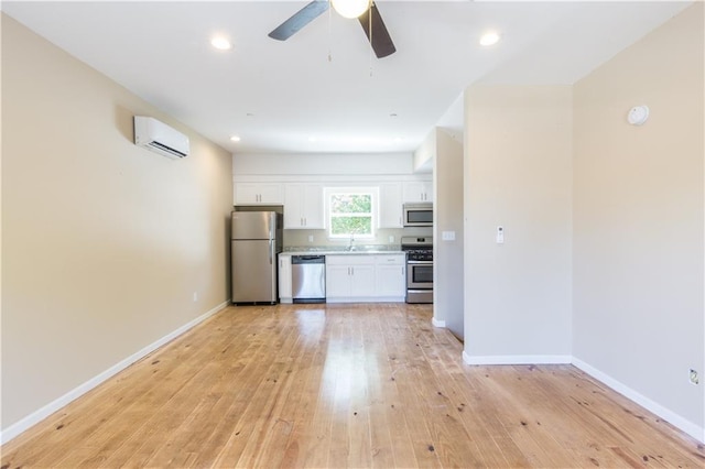 kitchen with white cabinets, appliances with stainless steel finishes, light hardwood / wood-style flooring, and a wall mounted AC