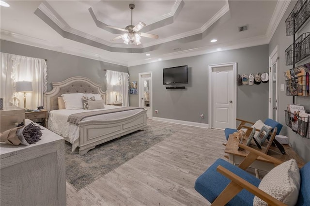 bedroom featuring ensuite bathroom, light hardwood / wood-style flooring, ceiling fan, ornamental molding, and a tray ceiling