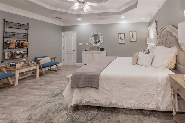 bedroom with ceiling fan, ornamental molding, a tray ceiling, and light hardwood / wood-style flooring