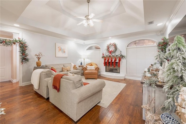 living room with a tray ceiling, ceiling fan, dark hardwood / wood-style flooring, and crown molding