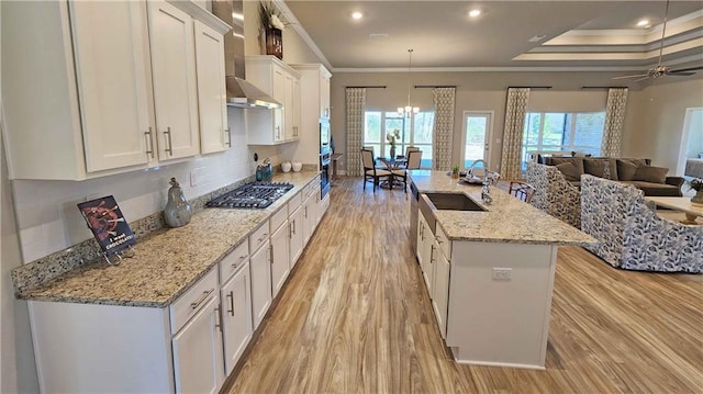 kitchen with appliances with stainless steel finishes, a center island with sink, white cabinetry, and wall chimney exhaust hood