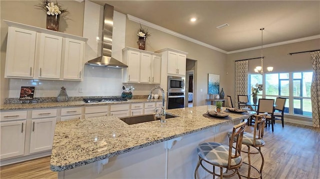 kitchen with stainless steel appliances, sink, wall chimney range hood, decorative light fixtures, and white cabinets