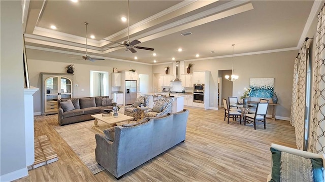 living room featuring ceiling fan with notable chandelier, light wood-type flooring, a tray ceiling, and ornamental molding