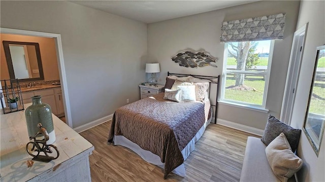 bedroom with ensuite bath, sink, and light wood-type flooring