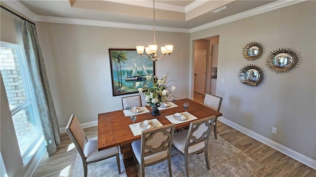 dining space featuring a tray ceiling, crown molding, wood-type flooring, and an inviting chandelier