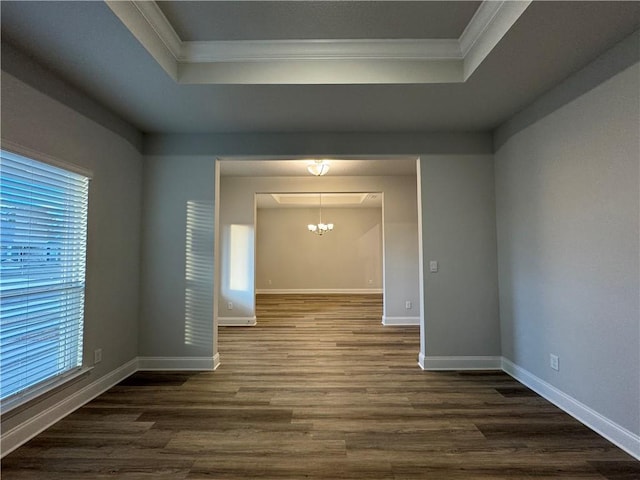 empty room featuring a notable chandelier, dark hardwood / wood-style floors, a raised ceiling, and ornamental molding