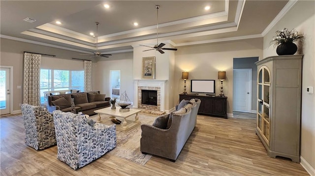 living room featuring a raised ceiling, ornamental molding, light wood-type flooring, and a brick fireplace