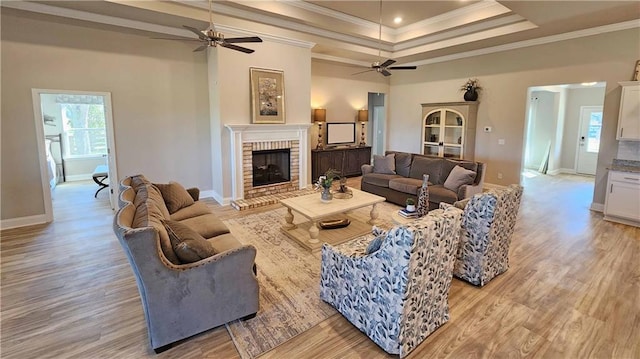 living room with a brick fireplace, ceiling fan, ornamental molding, and light wood-type flooring