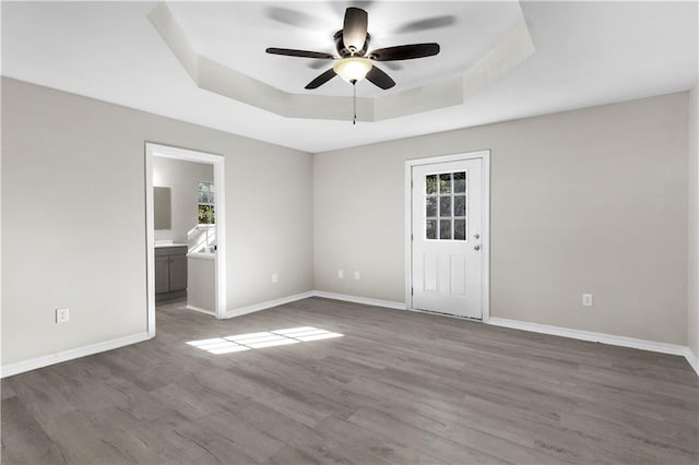 spare room with a tray ceiling, ceiling fan, hardwood / wood-style floors, and a healthy amount of sunlight