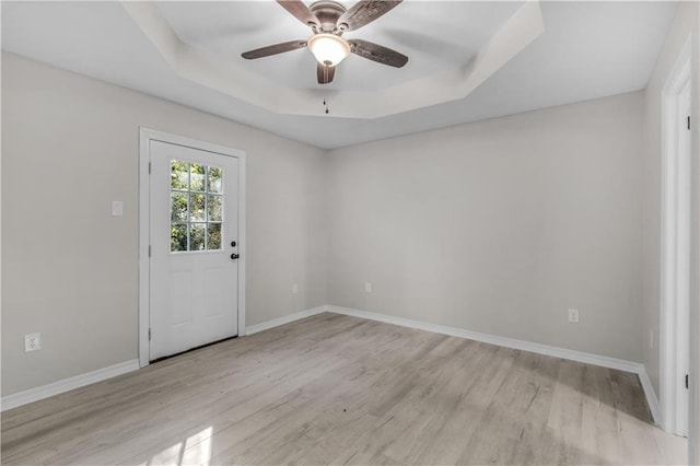 empty room with ceiling fan, light wood-type flooring, and a tray ceiling