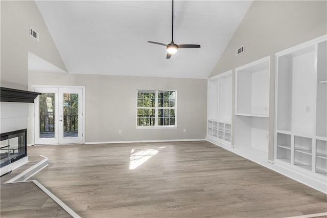 unfurnished living room with a tiled fireplace, high vaulted ceiling, a healthy amount of sunlight, and light hardwood / wood-style floors