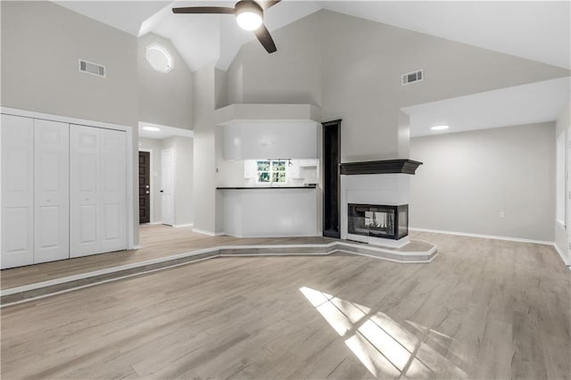 unfurnished living room featuring ceiling fan, a multi sided fireplace, light wood-type flooring, and high vaulted ceiling