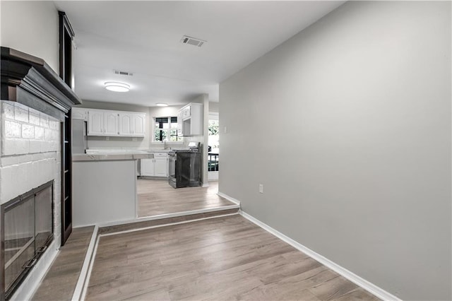 kitchen featuring black stove, a brick fireplace, light hardwood / wood-style flooring, kitchen peninsula, and white cabinets