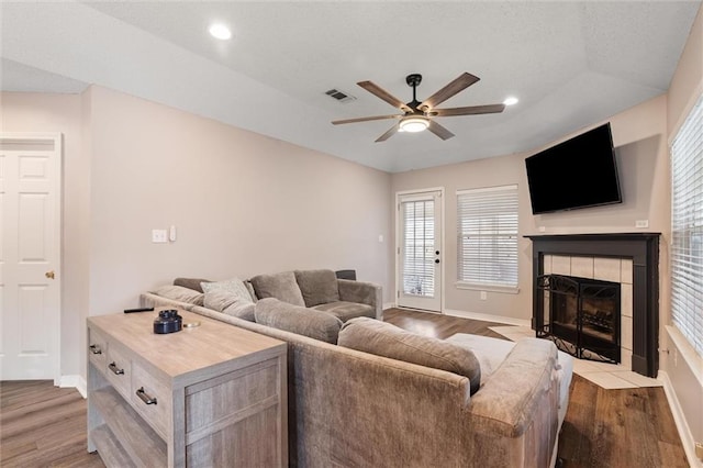 living area with a tray ceiling, visible vents, wood finished floors, and a ceiling fan