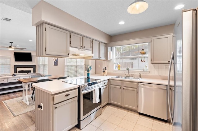 kitchen featuring visible vents, a peninsula, a sink, under cabinet range hood, and appliances with stainless steel finishes