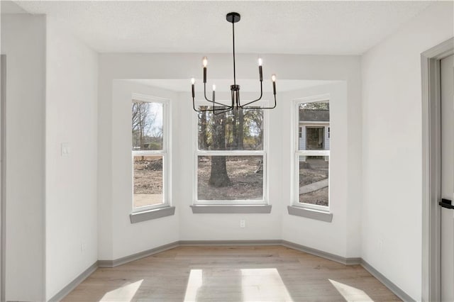 unfurnished dining area with a textured ceiling, an inviting chandelier, and light hardwood / wood-style flooring