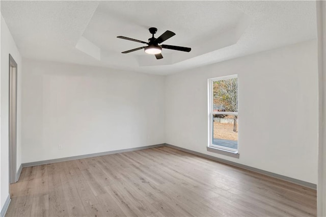 empty room with ceiling fan, light wood-type flooring, and a tray ceiling