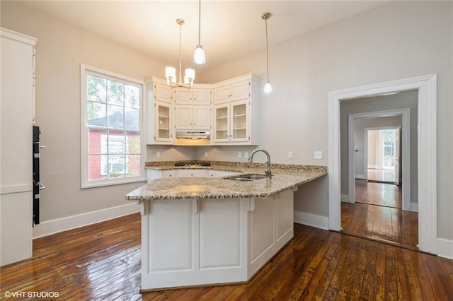 kitchen with kitchen peninsula, light stone countertops, sink, white cabinets, and hanging light fixtures