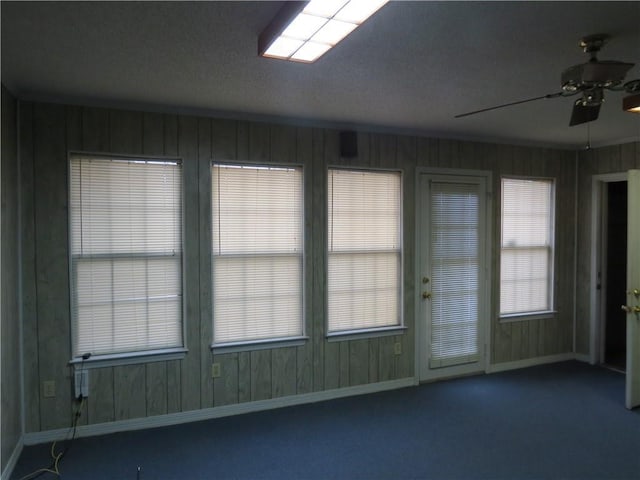 empty room with ceiling fan, carpet flooring, and wooden walls