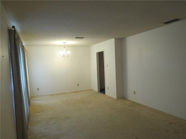 spare room featuring light carpet, a chandelier, and a textured ceiling