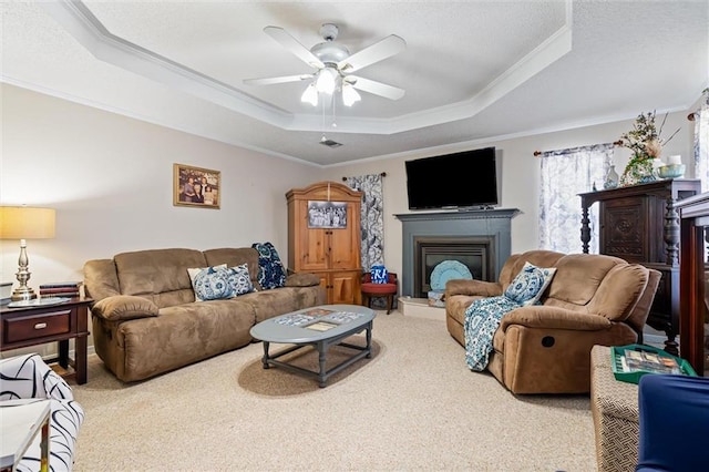 living room with a fireplace with raised hearth, crown molding, carpet, and a tray ceiling