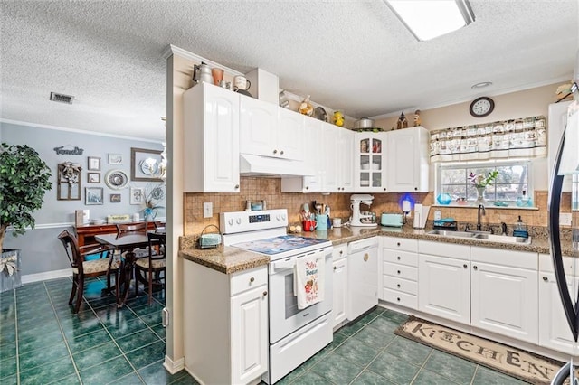 kitchen featuring dark tile patterned flooring, under cabinet range hood, a sink, white appliances, and crown molding