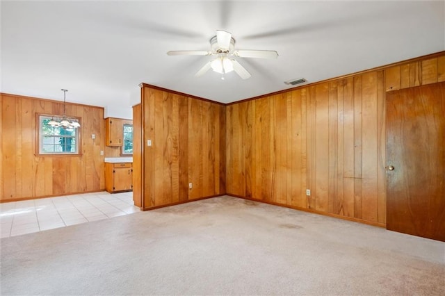 carpeted empty room featuring wooden walls, crown molding, and ceiling fan