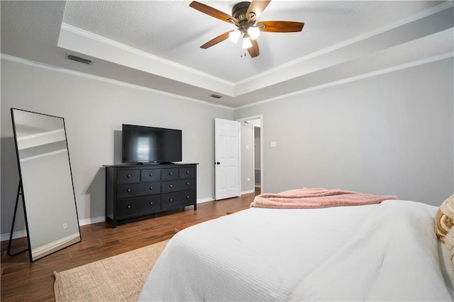 bedroom featuring dark wood-type flooring, visible vents, baseboards, ornamental molding, and a tray ceiling