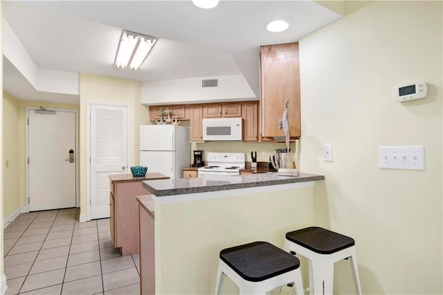 kitchen with light tile patterned floors, visible vents, a kitchen bar, white appliances, and a peninsula