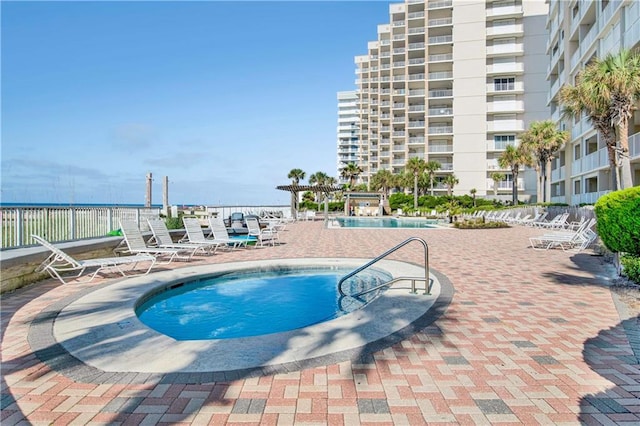 pool with fence, a water view, and a patio area