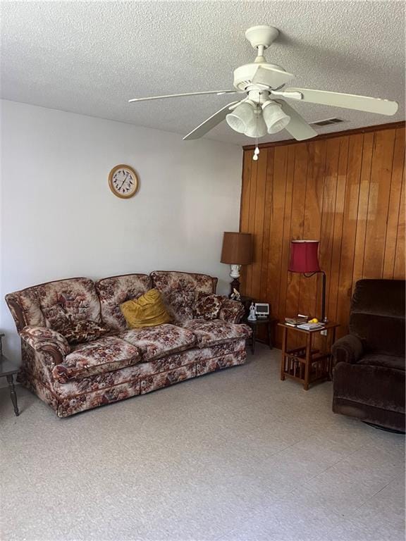 living room with wood walls, ceiling fan, and a textured ceiling