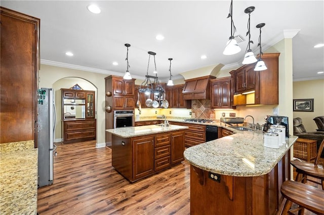 kitchen with stainless steel appliances, hardwood / wood-style flooring, a center island with sink, sink, and hanging light fixtures