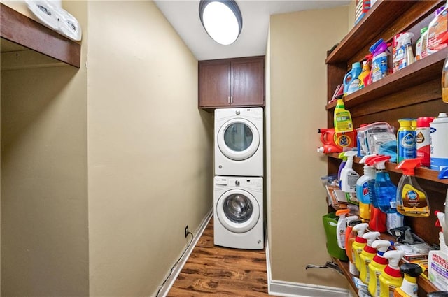 laundry room featuring cabinets, stacked washer and clothes dryer, and dark hardwood / wood-style flooring