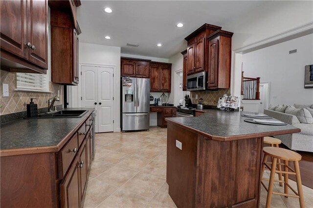 kitchen with light tile patterned floors, appliances with stainless steel finishes, tasteful backsplash, a breakfast bar, and sink