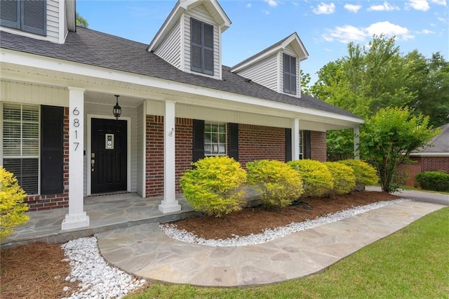 view of exterior entry with brick siding, a porch, and a shingled roof
