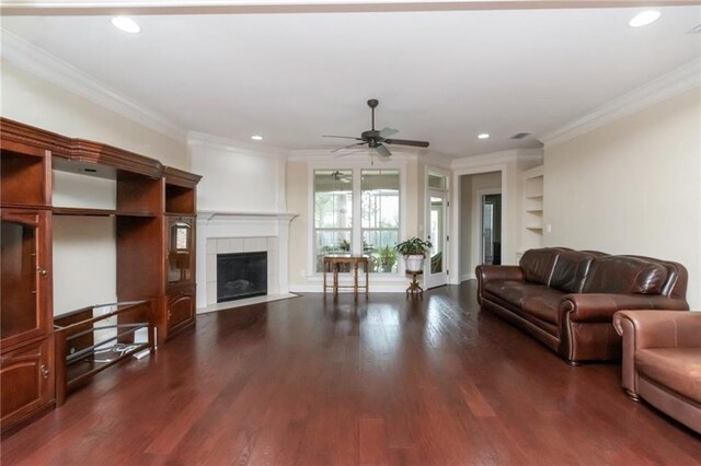 living room with dark wood-style flooring, a tiled fireplace, and crown molding