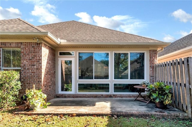 exterior space with a shingled roof, brick siding, fence, and a patio