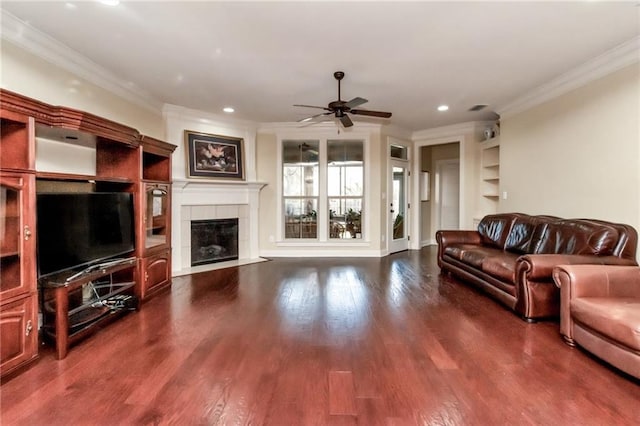 living room with a ceiling fan, ornamental molding, dark wood-style flooring, and a tile fireplace