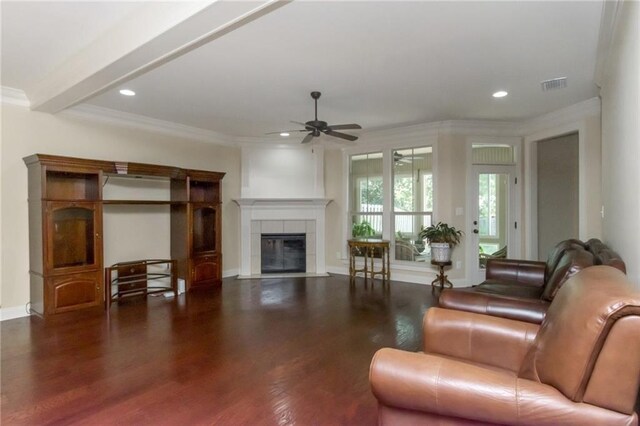 living room featuring a tile fireplace, beamed ceiling, dark wood-type flooring, ceiling fan, and ornamental molding