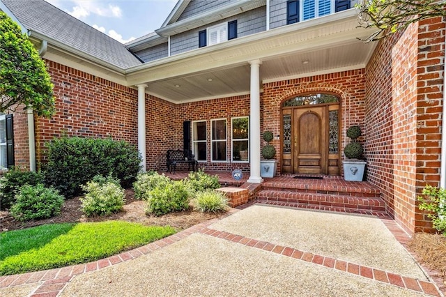 property entrance featuring brick siding, a porch, and roof with shingles