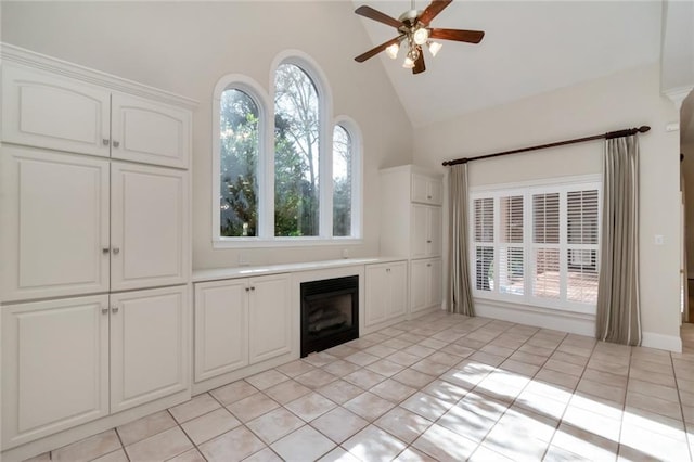 unfurnished living room featuring a wealth of natural light, high vaulted ceiling, a glass covered fireplace, and ceiling fan