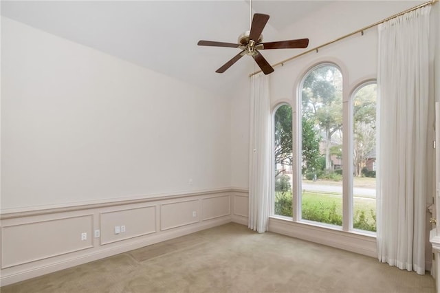 carpeted empty room featuring a decorative wall, ceiling fan, wainscoting, and vaulted ceiling